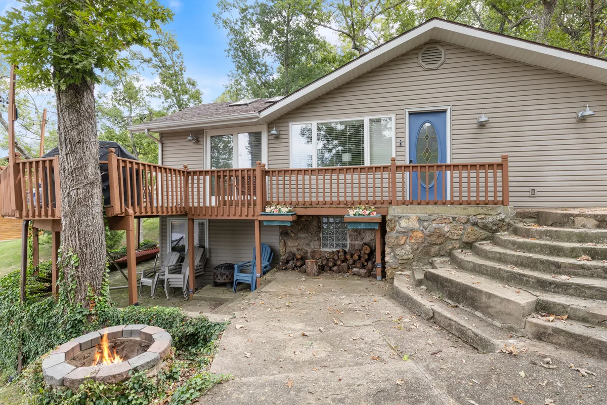 A wooden deck with a fire pit, stone steps, and large windows, set amidst greenery. The deck beckons for gatherings, relaxation, and enjoying both the architectural details and the surrounding landscape.
