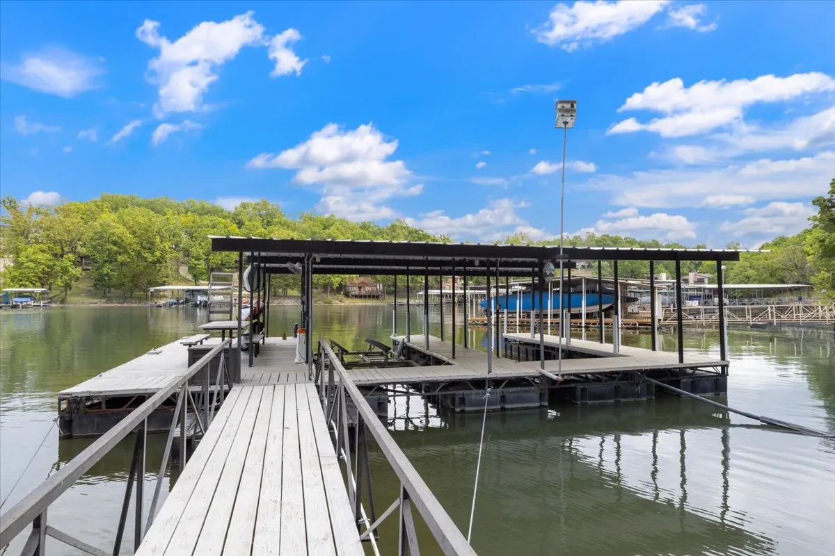 A peaceful wooden dock with multiple boat slips stretches out over calm lake waters, surrounded by lush green trees. The scene exudes tranquility and invites activities such as fishing, boating, and relaxing by the water. The serenity of the cove and the private dock access are clearly visible.