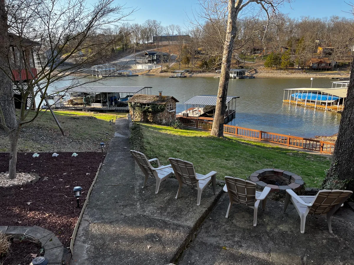 A tranquil lakeside patio area with Adirondack chairs arranged around a fire pit, overlooking the water. Patio seating and grassy lawn extend to the lake’s edge, creating an inviting space for morning coffee, evening fireside chats, and stargazing.