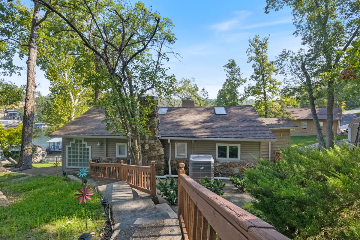 A charming house facade with classic stone chimney, wooden walkway, lush greenery, and a decorative flower sculpture. The exterior speaks to the blend of historic stonework and welcoming warmth, with hints of vintage design and modern upkeep.
