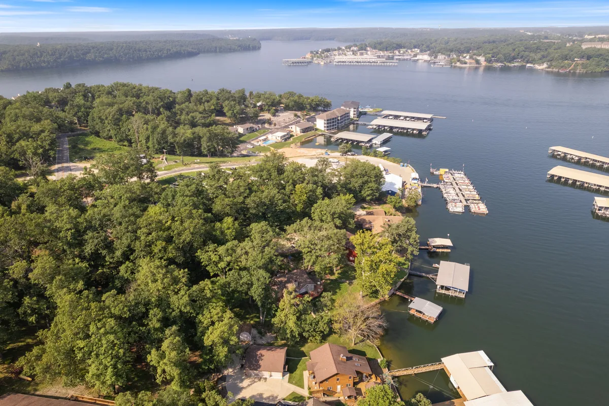 A sweeping view of the lake featuring a marina, docks, forested shoreline, and nearby residential homes. The scene is vibrant and inviting, with boats docked and ready for adventure, all framed by the expansive water and green landscape.