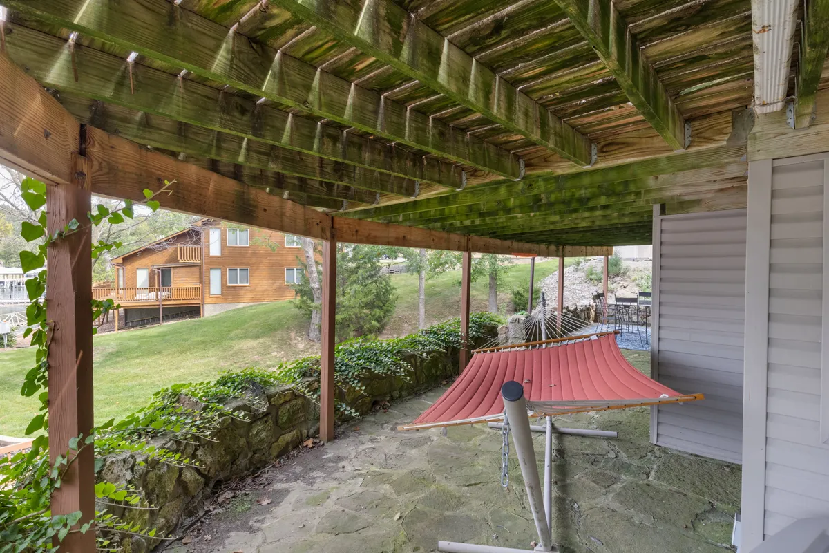 A hammock is gently suspended under a wooden pergola atop a stone patio, framed by greenery. The space feels secluded and peaceful, perfect for reading, napping, or unwinding while enjoying nature.