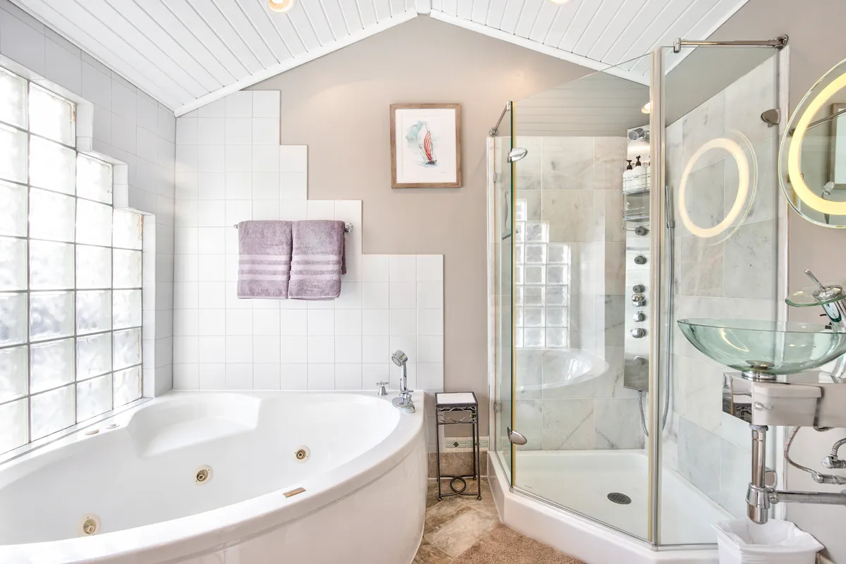 A serene bathroom featuring an oversized jacuzzi tub, a glass shower enclosure, soft towels, and framed artwork. Natural light brightens the space, creating a spa-like atmosphere.