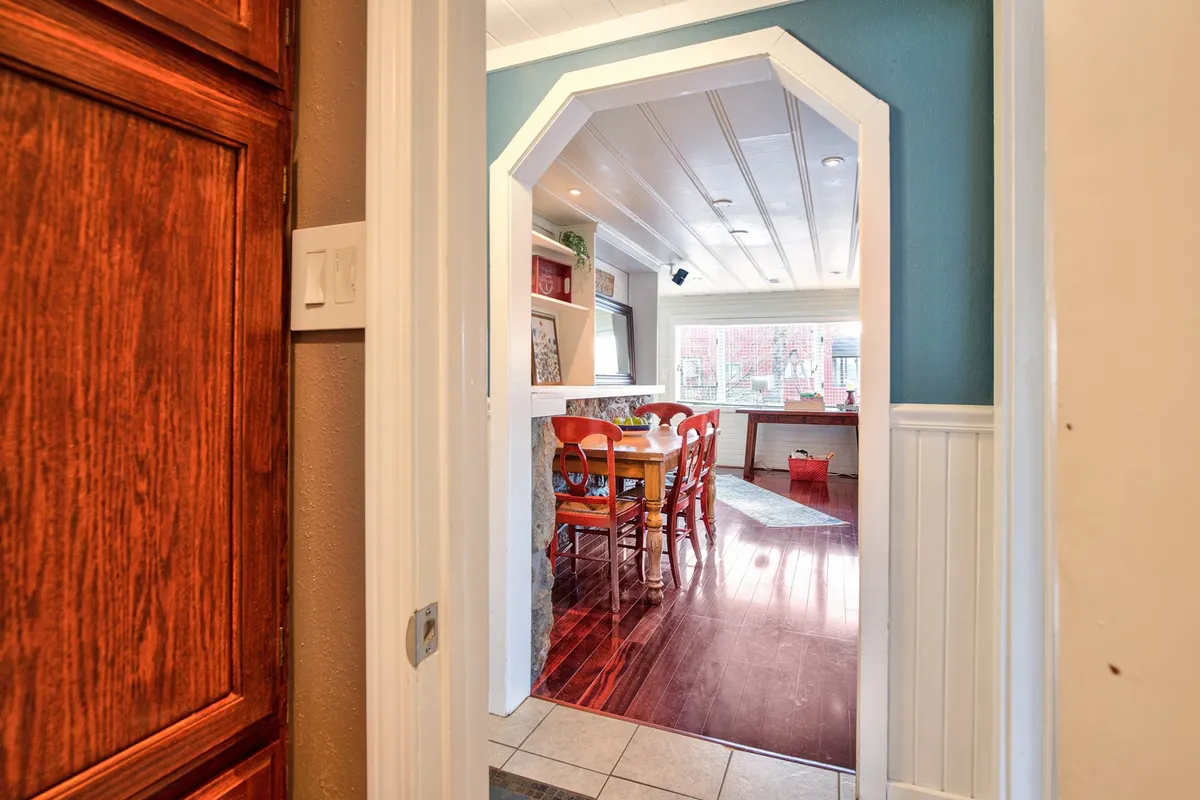A cozy dining nook marked by an arched doorway, a wooden dining table, and vivid red chairs. The warm lighting and intimate setup suggest a perfect spot for shared meals, holiday gatherings, and board games, embodying the hospitality and nostalgia of the home.