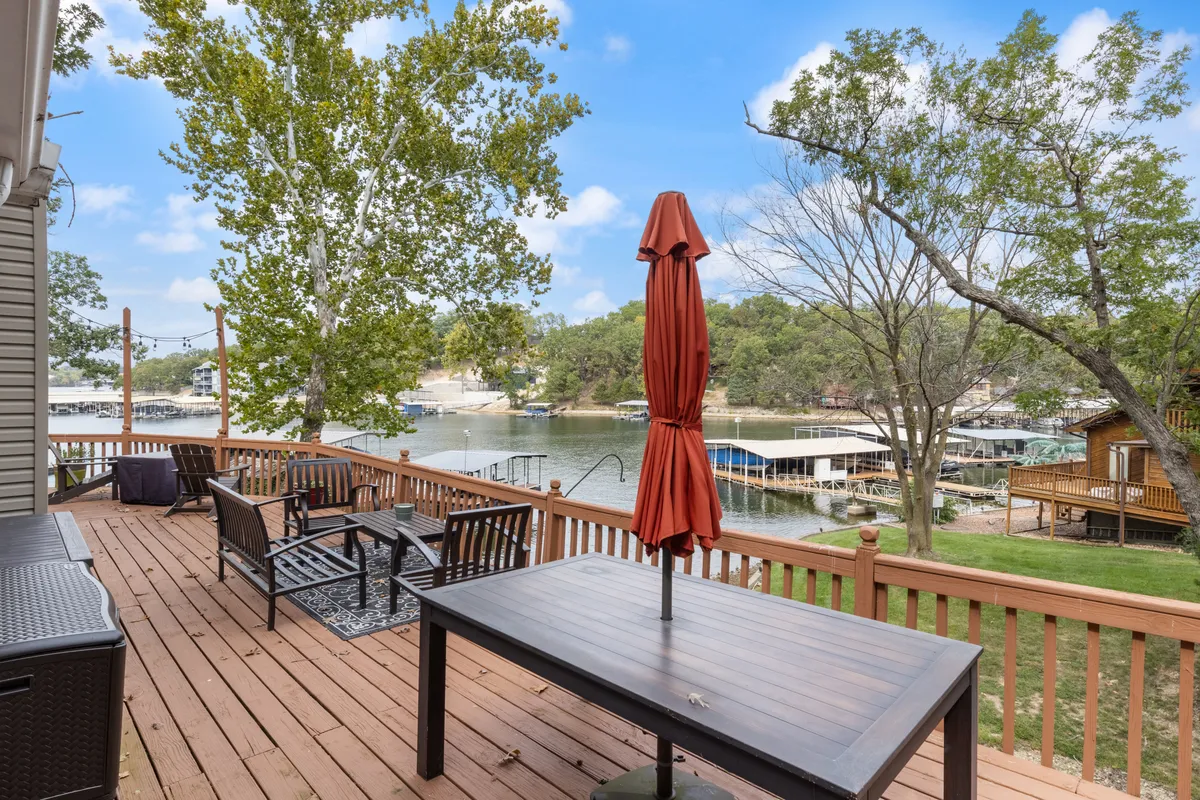 A spacious wooden deck with an outdoor dining table, red umbrella, lounge chairs, and views overlooking the water. The deck is set for relaxation and social gatherings, seamlessly blending the comfort of home with the beauty of lakeside nature.