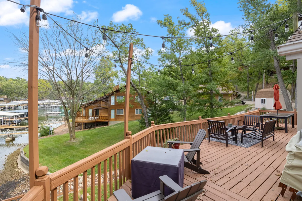 A spacious wooden deck with comfortable seating, string lights, and a beautiful view overlooking the tranquil lake and surrounding trees. The inviting setup encourages outdoor relaxation, dining, and unwinding after a day on the water.