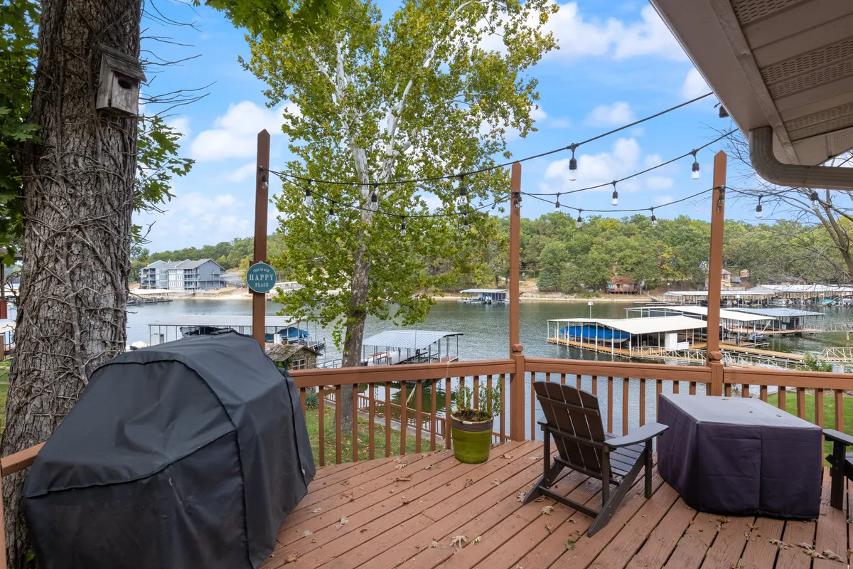 A lively lakefront deck featuring a grill, wooden deck area, hanging lights, and a panoramic view of the water. The setup is primed for outdoor dining, summer parties, or quiet mornings with coffee—showcasing both the natural beauty and the social possibilities.