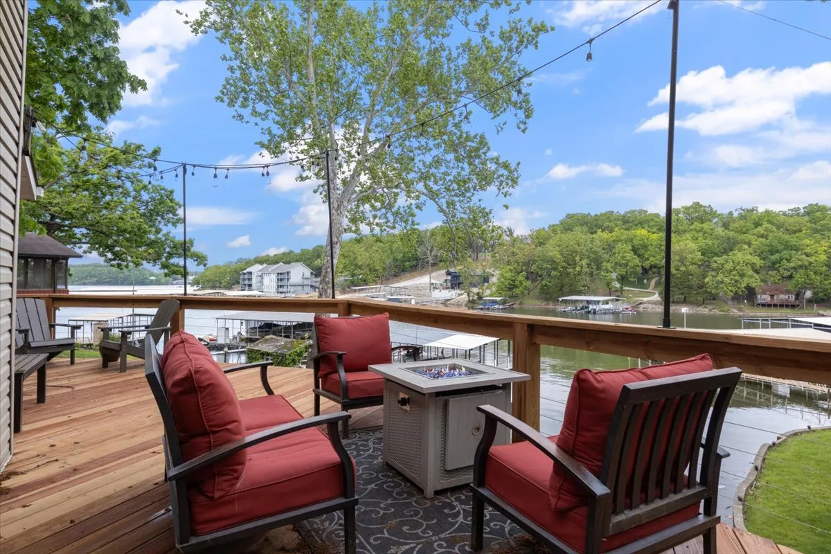 The image features a cozy outdoor seating area with plush red-cushioned chairs gathered around a round coffee table, all set beneath string lights with a stunning view of the lake. The scene is perfect for evening gatherings or peaceful mornings, inviting guests to relax, socialize, and soak in lakeside serenity.