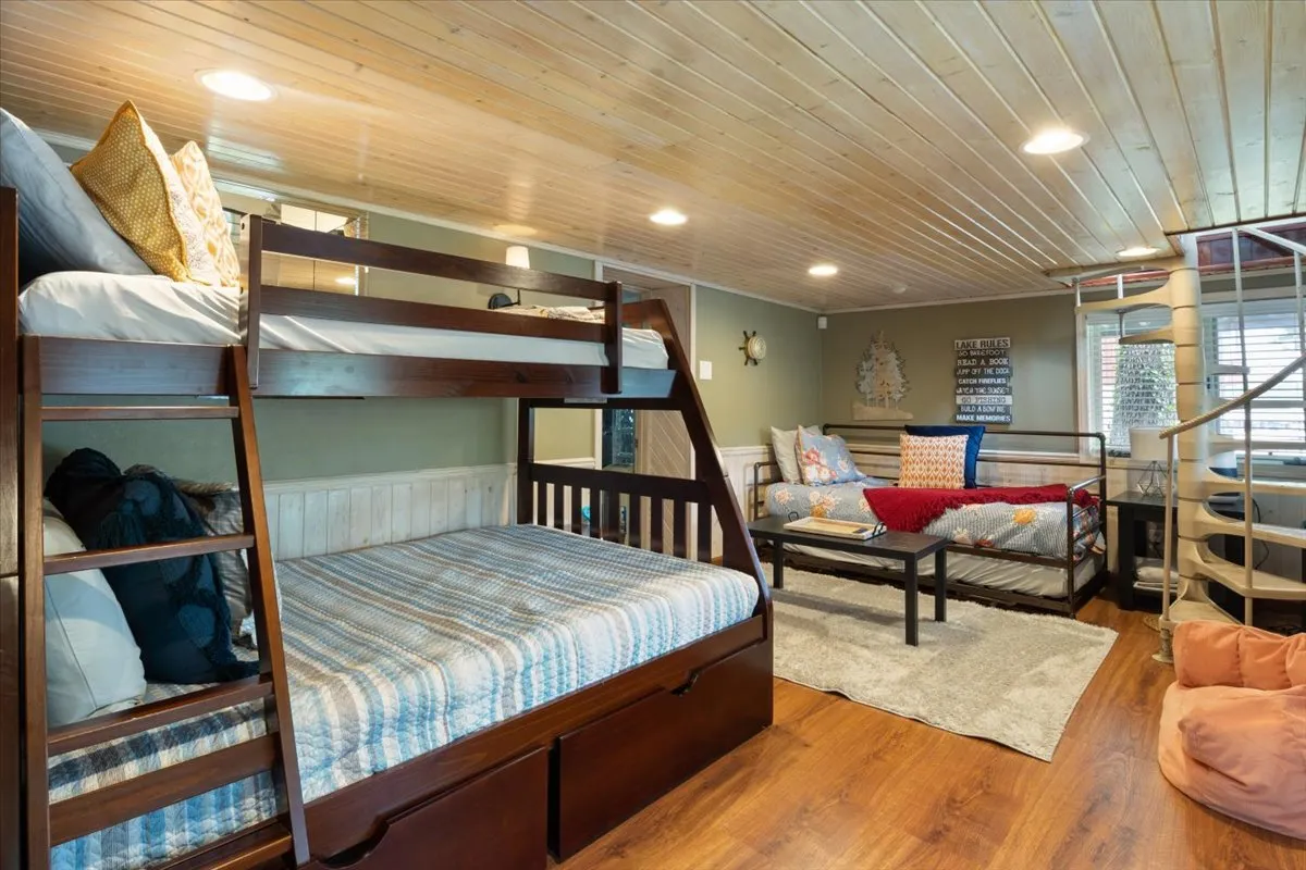 A playful, family-friendly bedroom with bunk beds, a daybed, decorative pillows, an area rug, and a warm wooden ceiling. The space is ideal for kids or friends, offering flexibility and a welcoming mood.